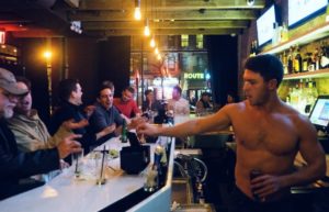 shirtless male bartender pouring a drink